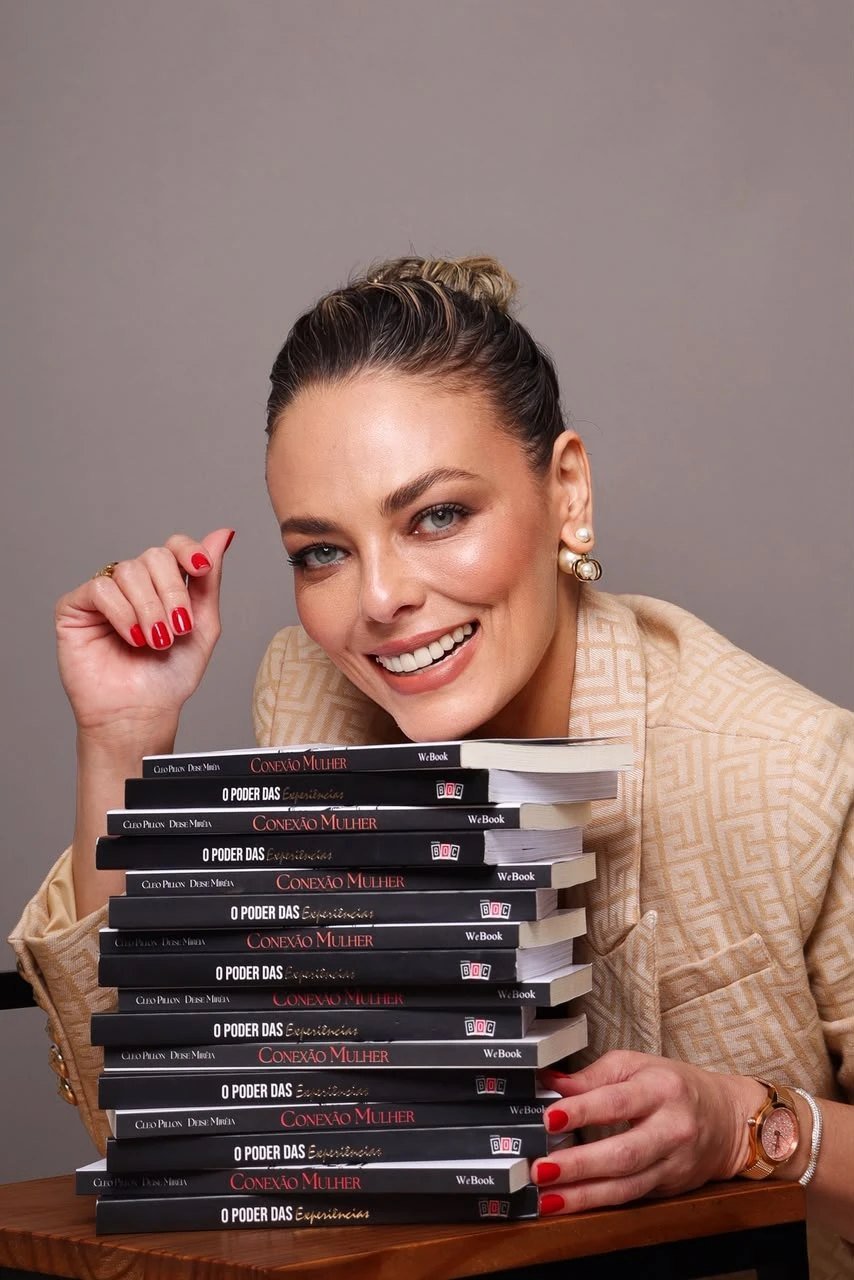 Deise Miréia sorrindo, apoiada em uma pilha dos livros O Poder das Experiências e Conexão Mulher